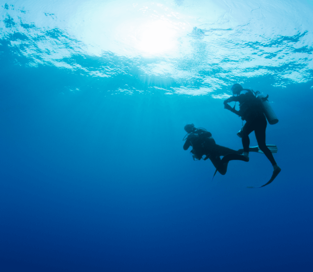 Deux plongeurs en autonomie évoluant sous la surface, silhouettes à contre-jour dans l'eau bleue